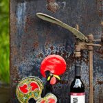 Photo of rooster sculpture next to a bottle of wine in a corking machine.